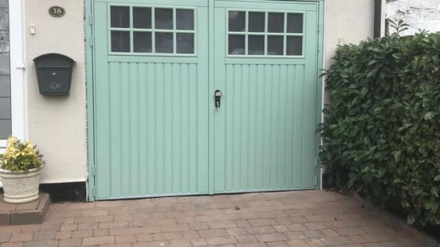 pale green side hined garage door instlled on pale pebble dash house